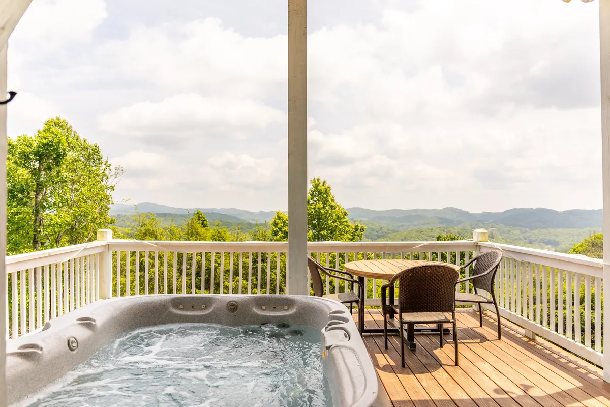 An inviting hot tub overlooks panoramic mountain views, accompanied by an outdoor dining table. The space is set up for both relaxation and socializing, with serene surroundings that invite stargazing and shared moments.