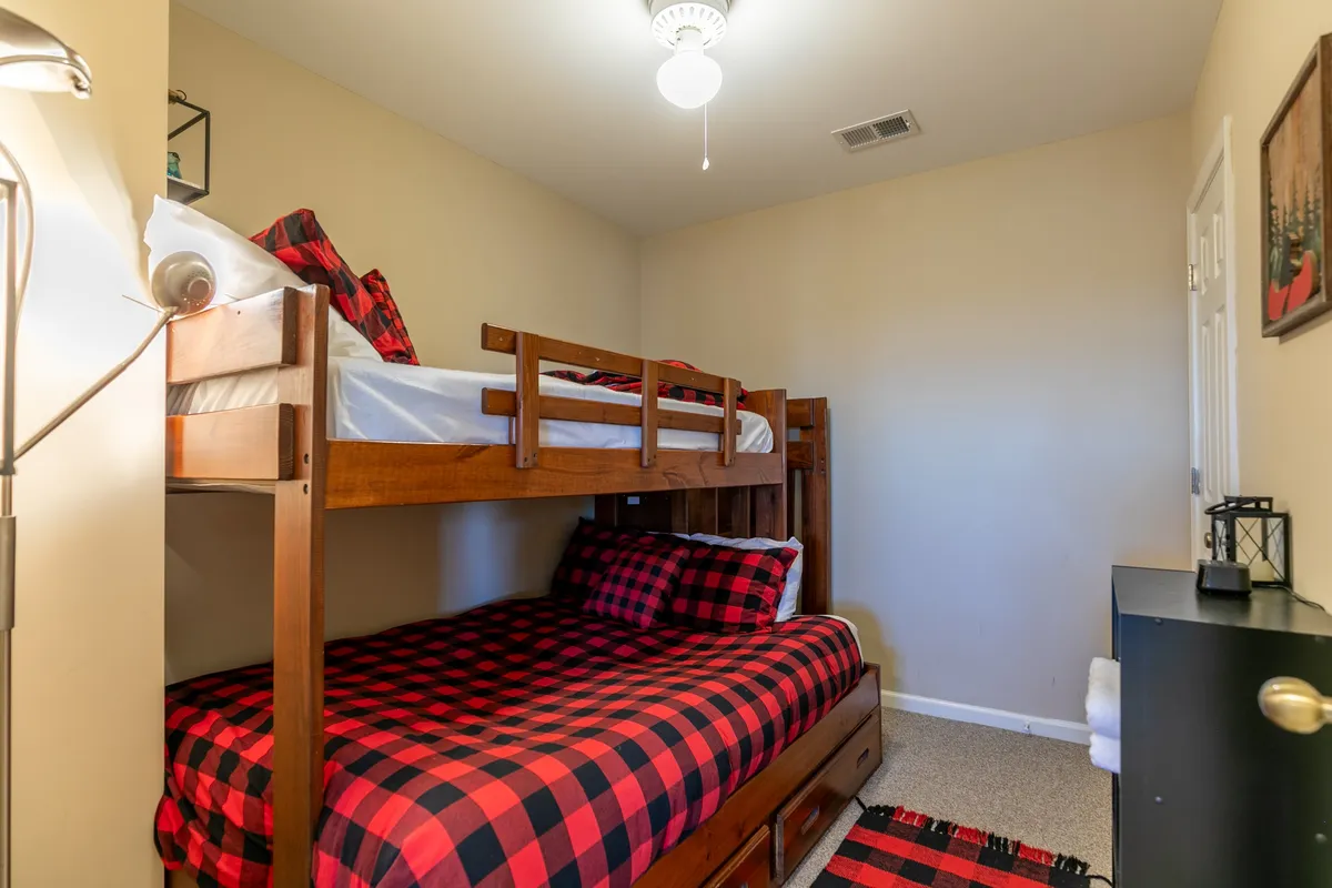 A comfortable bunk room with a twin-over-full bunk bed dressed in plaid bedding, a nightstand, and warm lighting. The space exudes a sense of coziness, perfect for kids to claim as their own for sleepovers or storytime.