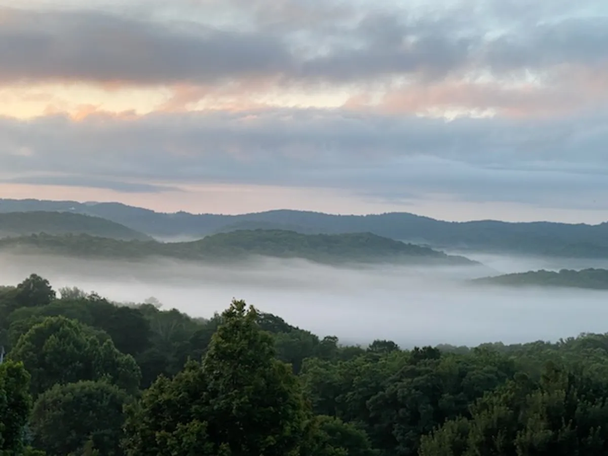 An inspiring landscape shot featuring rolling hills, mist-covered valleys, and a soft pastel sky. The focus is on the natural surroundings, evoking the adventure and serenity of the Blue Ridge region. This view invites exploration and captures the wonder of the area's hiking trails and mountain vistas.