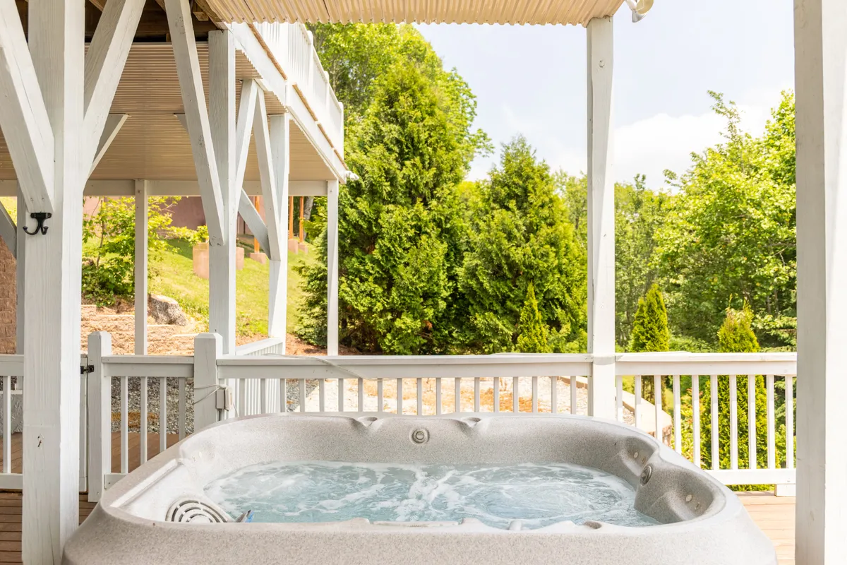 An outdoor hot tub nestled beside a wooden structure, surrounded by lush greenery. The area exudes seclusion and tranquility, inviting guests to relax and enjoy the natural beauty around them. The setting is perfect for stargazing at night or unwinding after a day of exploring the mountains.