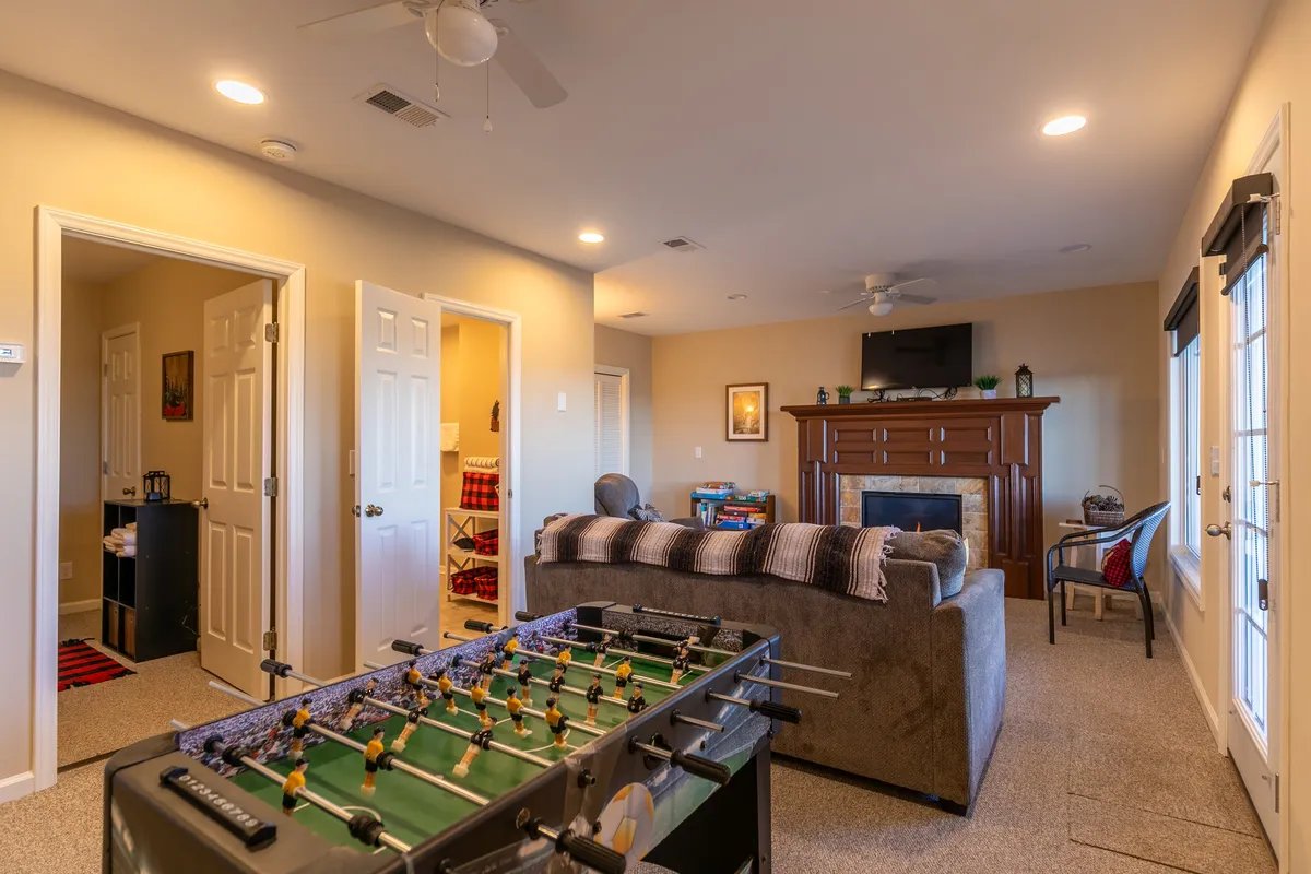 A cozy, casual den featuring a foosball table, a warm fireplace, a comfortable sofa, and a television. The setting is perfect for family game nights, movie marathons, and relaxed gatherings after an adventurous day outdoors.