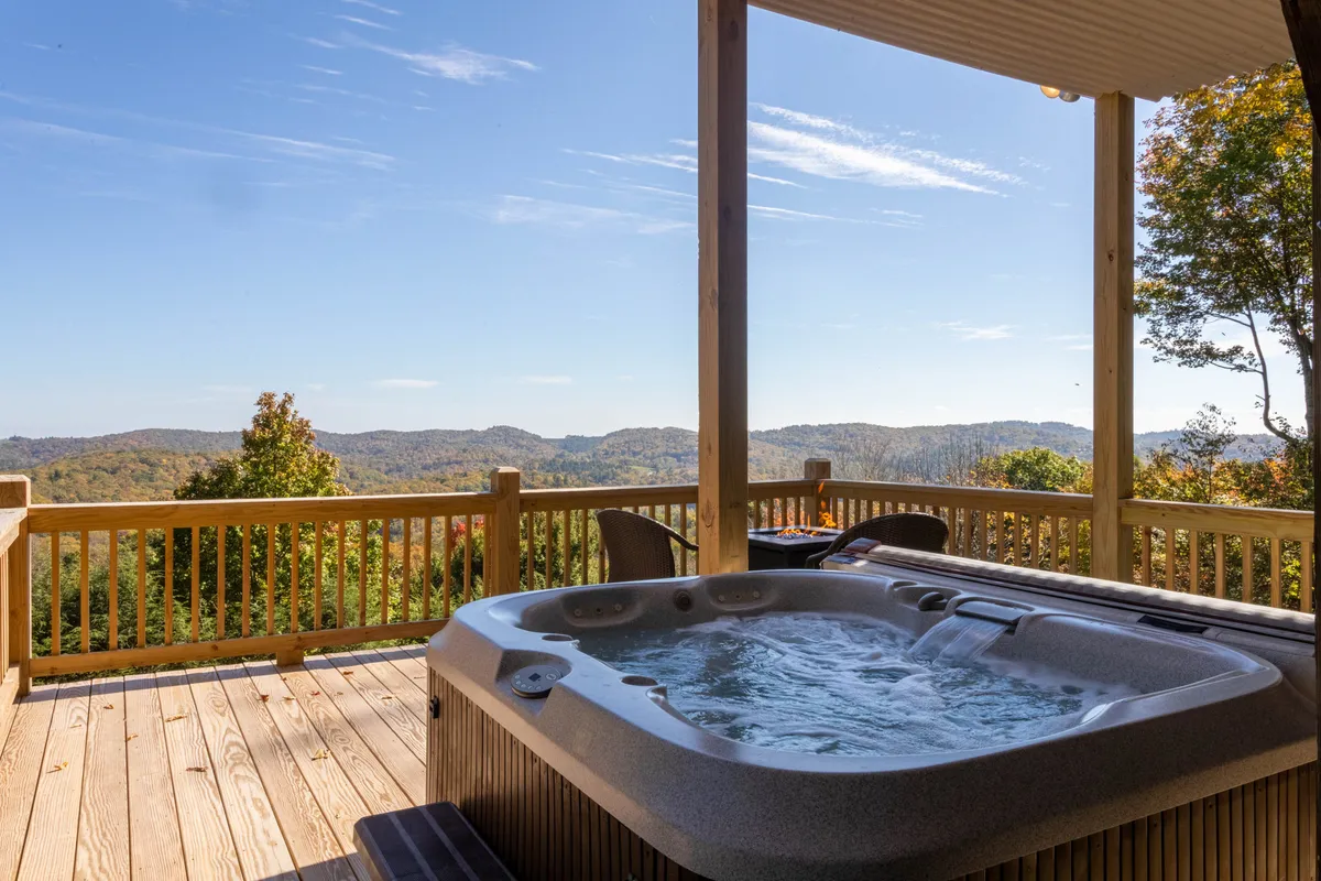 An inviting outdoor hot tub set on a wooden deck with seating and a panoramic mountain view. The space is designed for serene soaks under the stars, socializing, and enjoying the peaceful mountain atmosphere.
