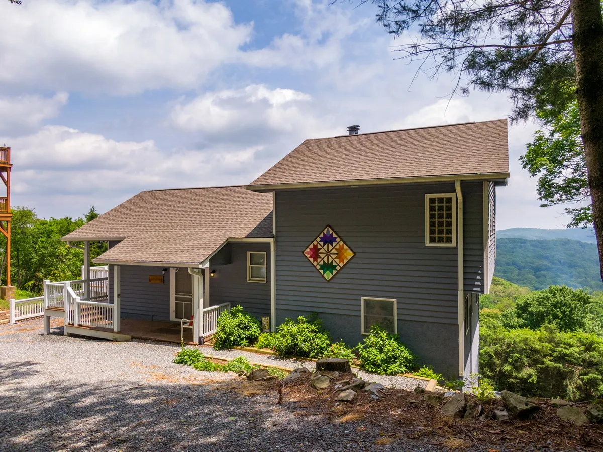 This exterior shot features the home's charming porch, the colorful quilt square on the side, surrounding greenery, and distant mountain views. The porch area looks inviting and connects immediately to the outdoors, suggesting a tranquil, pet-friendly place for arrival and relaxation.