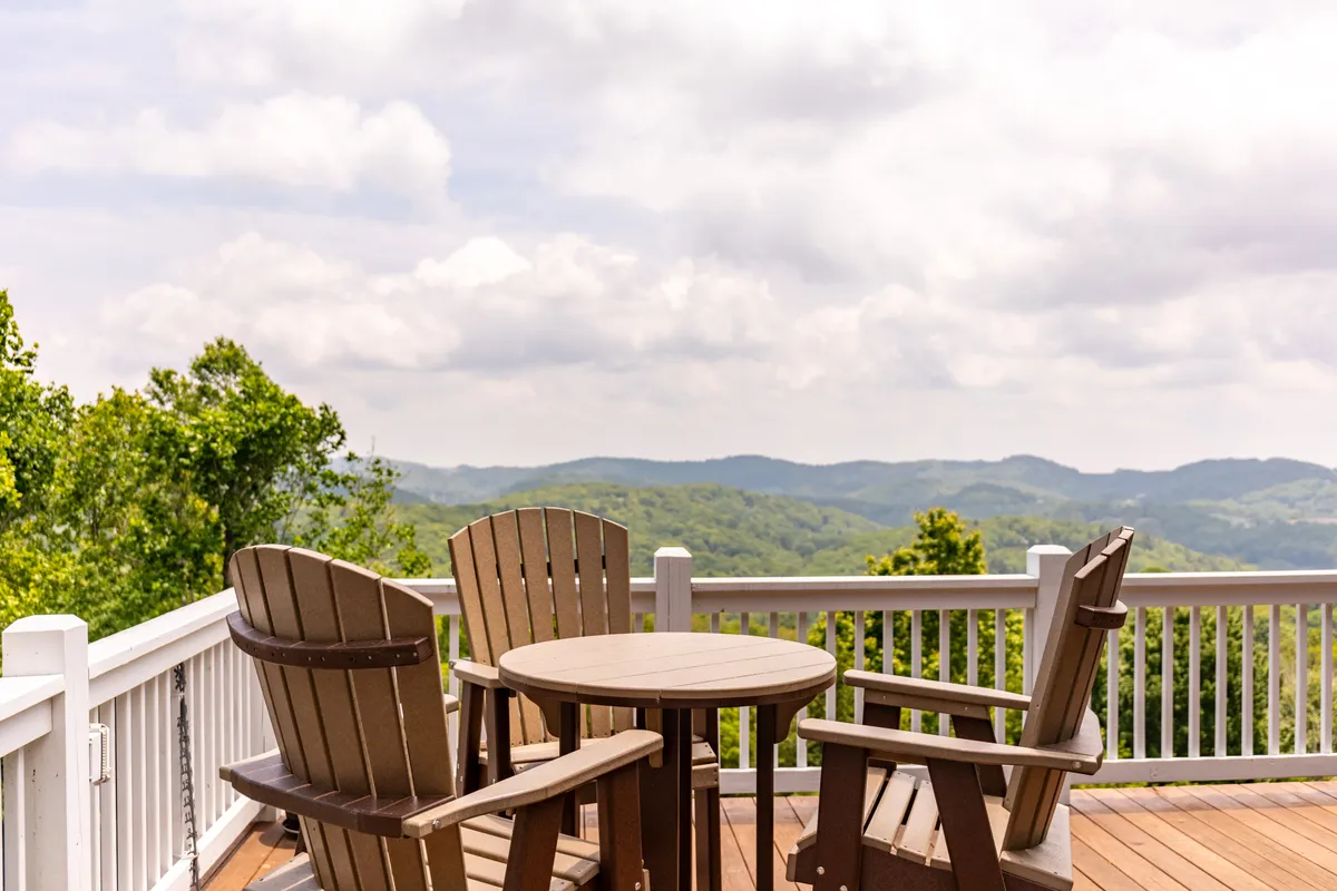 A cluster of Adirondack chairs surrounds a small round table, all oriented toward a breathtaking mountain view. The setting suggests a peaceful spot to sip coffee, read, or chat, with the distant mountains framing the experience.