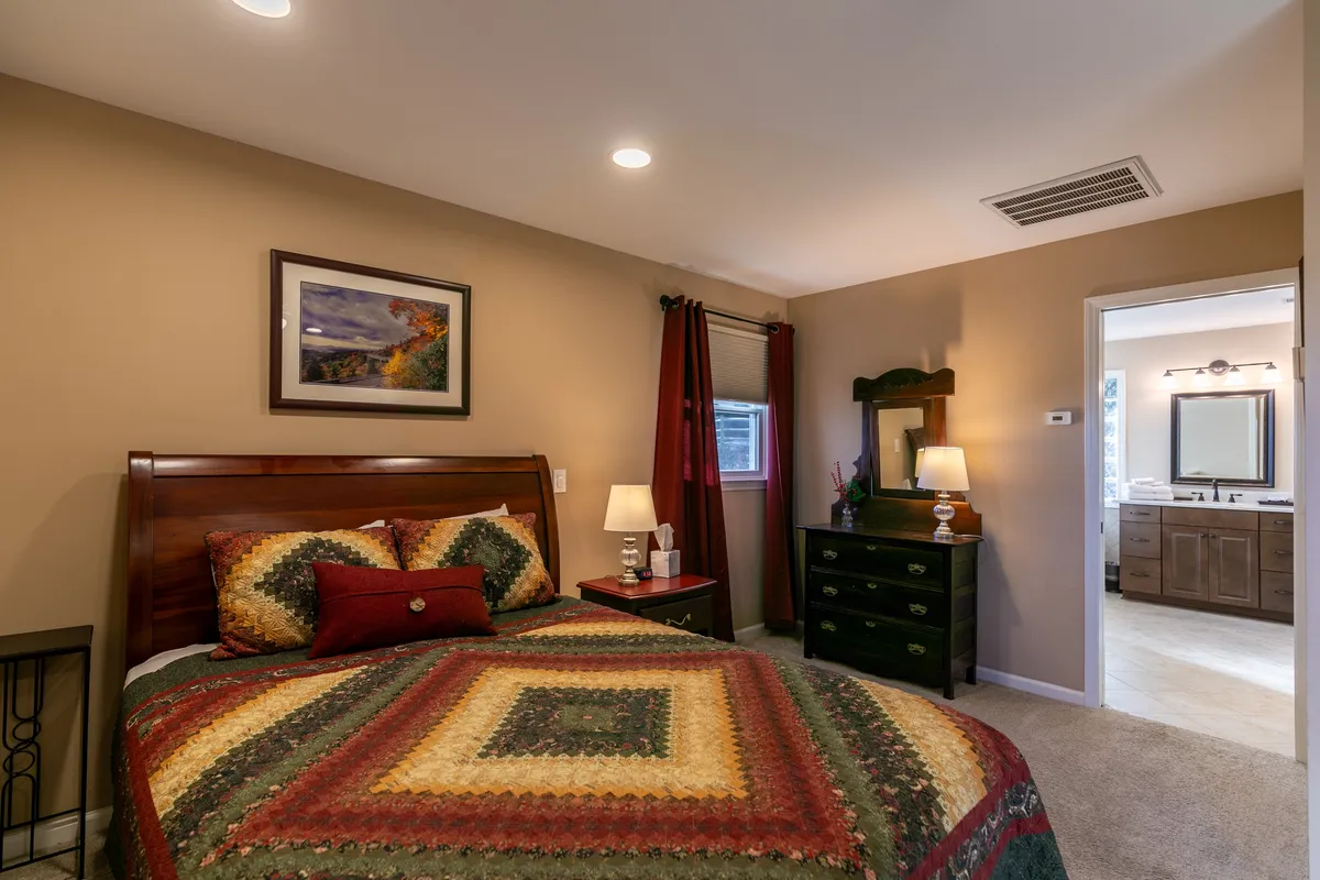 A comfortable queen bedroom with a quilted bedspread, wooden bed frame, nightstand with a glowing lamp, and framed artwork on the wall. The soft, homey ambiance makes it an inviting retreat for rest and privacy.
