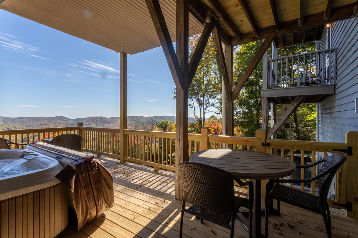 This exterior image captures a spacious deck featuring a bubbling hot tub, wooden railing, outdoor dining table, and a stunning panoramic view of the surrounding mountains. The space is inviting, offering both relaxation and social opportunities amid breathtaking natural beauty.